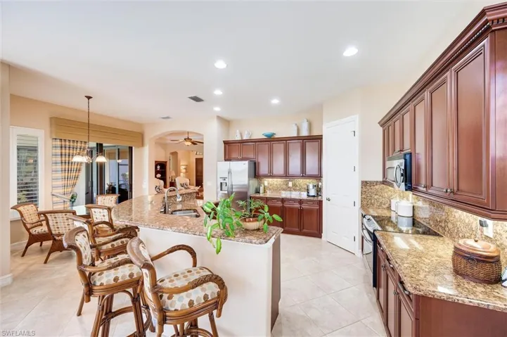Kitchen featuring a kitchen breakfast bar, stainless steel appliances, light stone counters, a ceiling fan, and a center island with sink