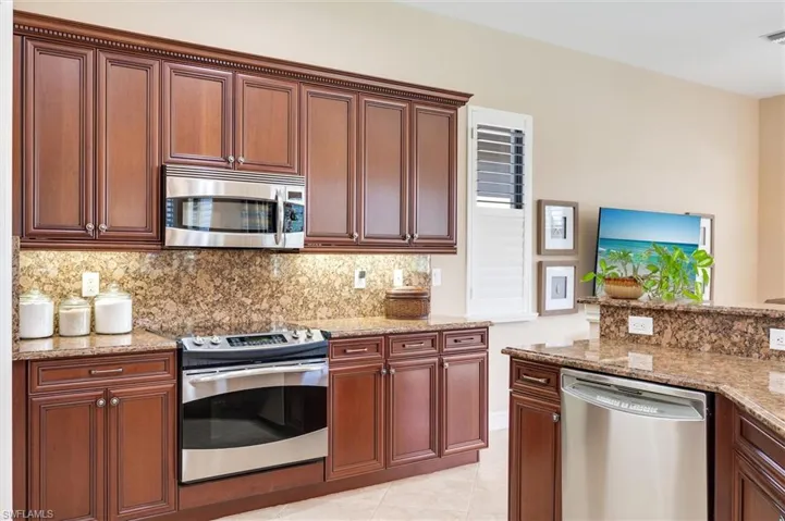 Kitchen with stainless steel appliances, light stone counters, light tile patterned floors, and tasteful backsplash
