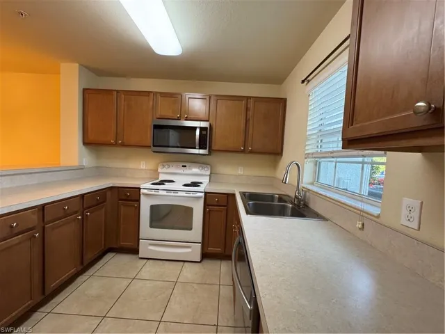 Kitchen featuring range, a sink, dishwasher, light countertops, and brown cabinets