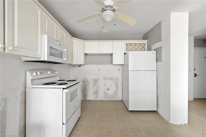 Kitchen with light tile patterned floors, ceiling fan, white appliances, and white cabinets