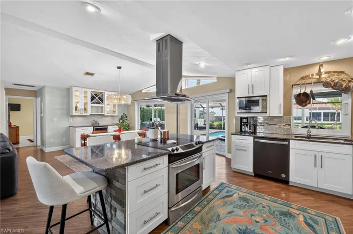 Kitchen with a kitchen breakfast bar, stainless steel appliances, vaulted ceiling, island exhaust hood, and white cabinetry