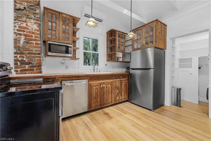 Kitchen with light hardwood / wood-style flooring, appliances with stainless steel finishes, hanging light fixtures, sink, and an AC wall unit
