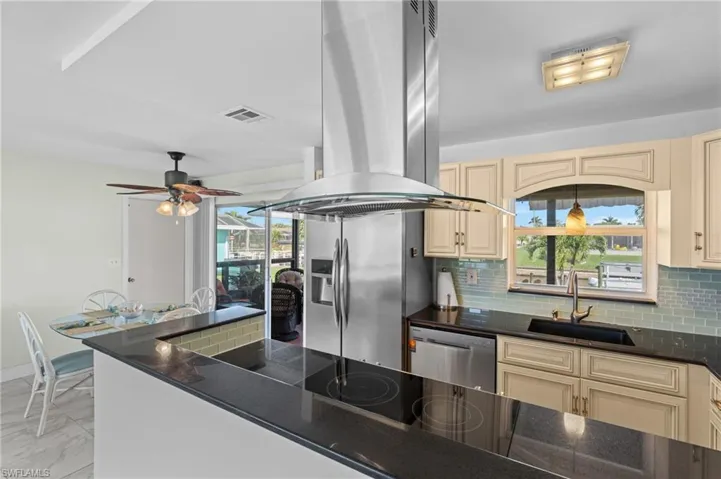 Kitchen with sink, appliances with stainless steel finishes, cream cabinets, and island range hood