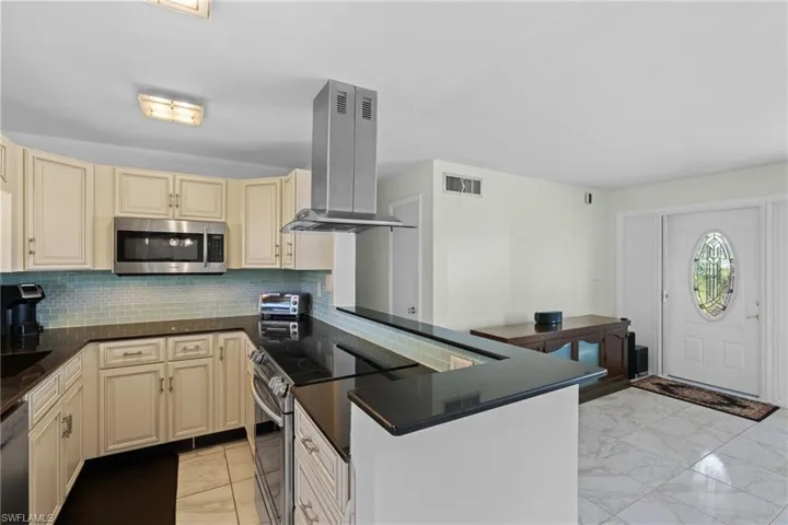Kitchen featuring island range hood, stainless steel appliances, backsplash, and kitchen peninsula