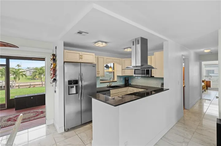 Kitchen with kitchen peninsula, sink, tasteful backsplash, appliances with stainless steel finishes, and island range hood