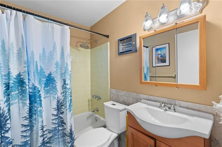Full bathroom with tile walls, vanity, toilet, and shower / bathtub combination with curtain