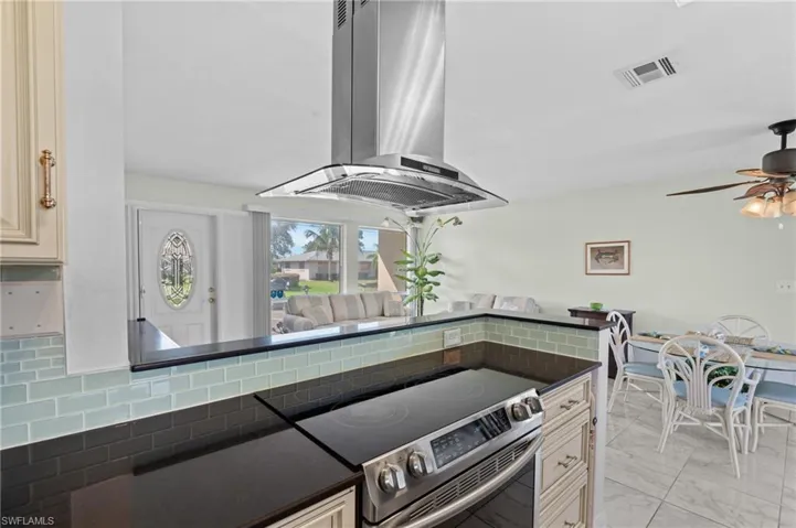 Kitchen featuring island exhaust hood, ceiling fan, stainless steel electric range, cream cabinets, and decorative backsplash