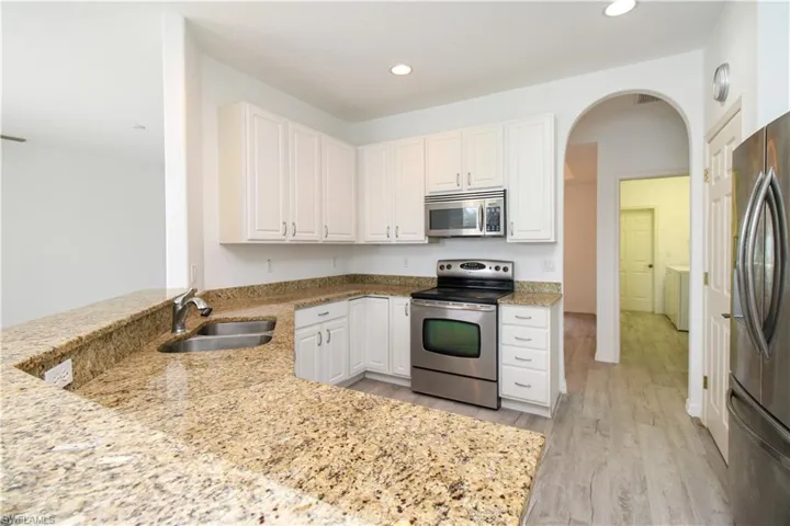 Kitchen featuring stainless steel appliances, arched walkways, light stone counters, a peninsula, and recessed lighting