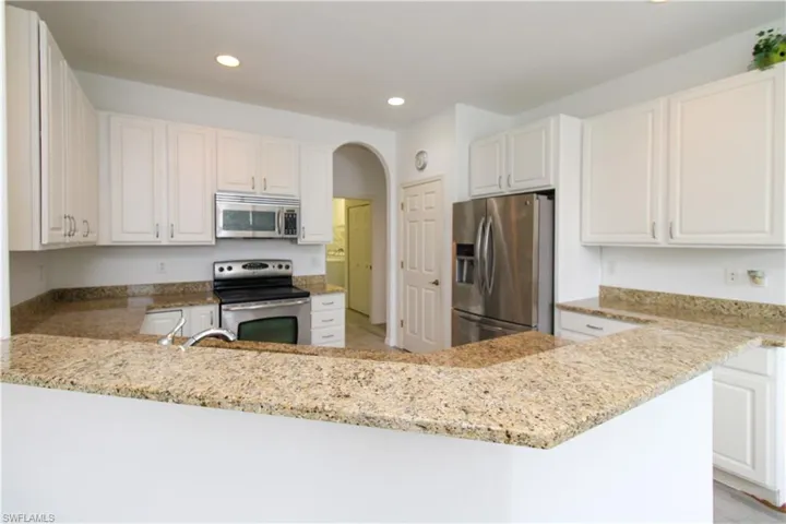 Kitchen featuring appliances with stainless steel finishes, white cabinets, light stone counters, recessed lighting, and arched walkways