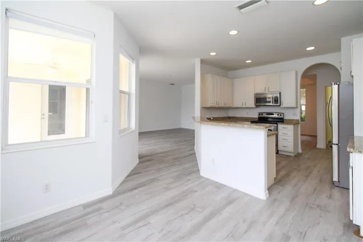 Kitchen featuring arched walkways, light stone countertops, stainless steel appliances, white cabinetry, and recessed lighting
