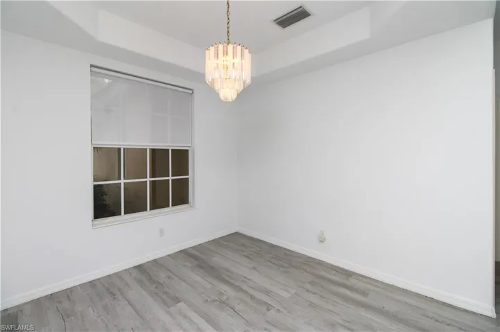 Unfurnished room with a raised ceiling, wood finished floors, and a chandelier