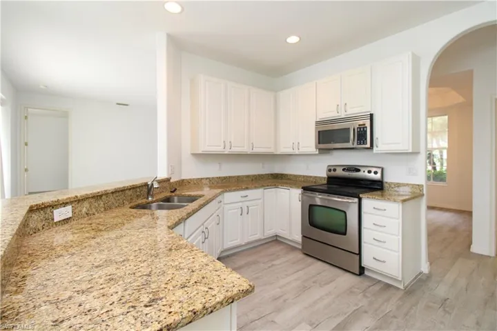 Kitchen featuring arched walkways, stainless steel appliances, white cabinets, a peninsula, and light stone countertops