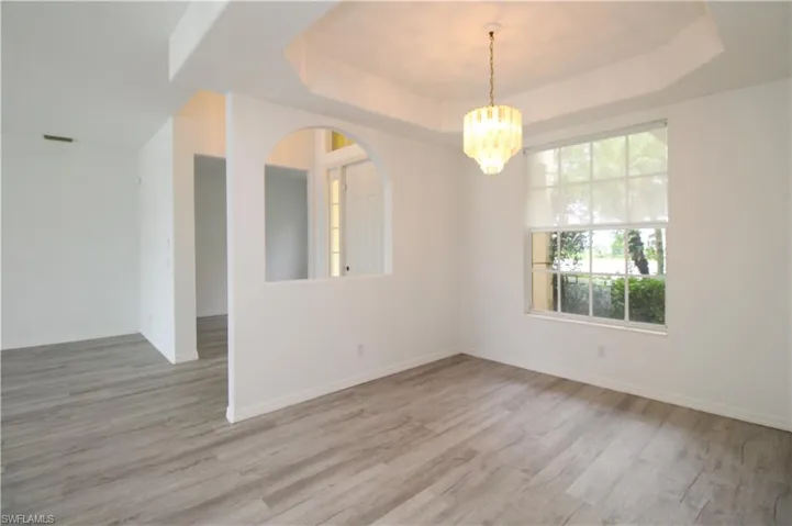 Unfurnished room with a chandelier, light wood-type flooring, and a raised ceiling