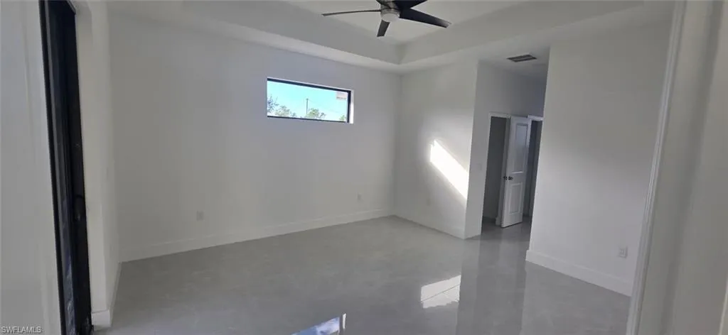 Unfurnished room with finished concrete flooring, a raised ceiling, and ceiling fan