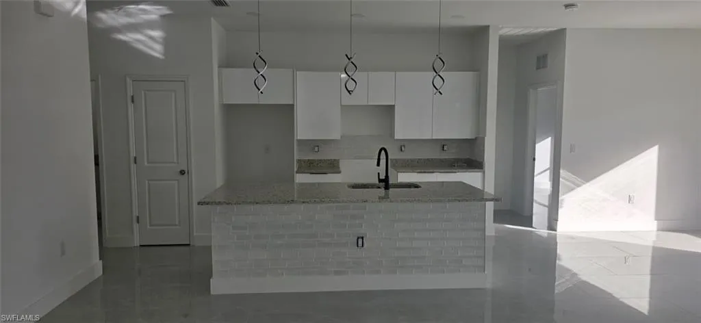 Kitchen with light stone countertops, white cabinetry, an island with sink, pendant lighting, and backsplash