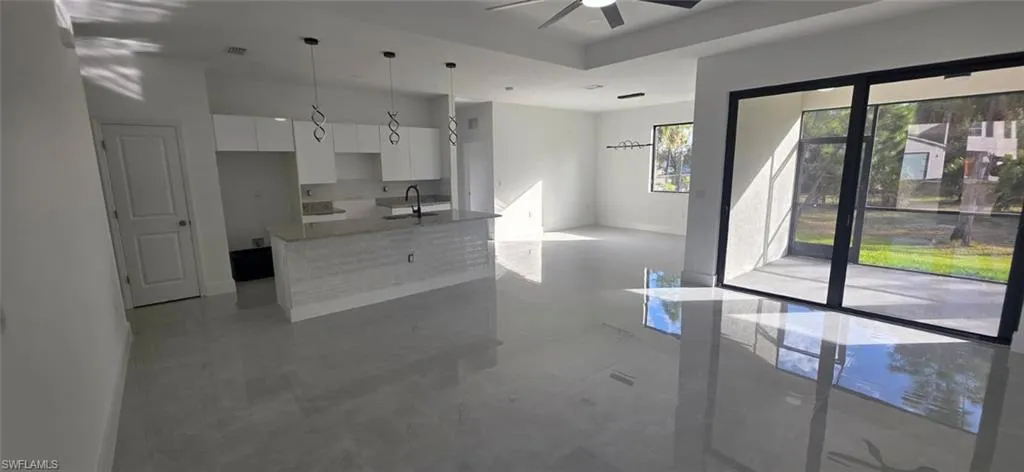 Kitchen featuring white cabinets, light stone countertops, a kitchen island with sink, pendant lighting, and a ceiling fan