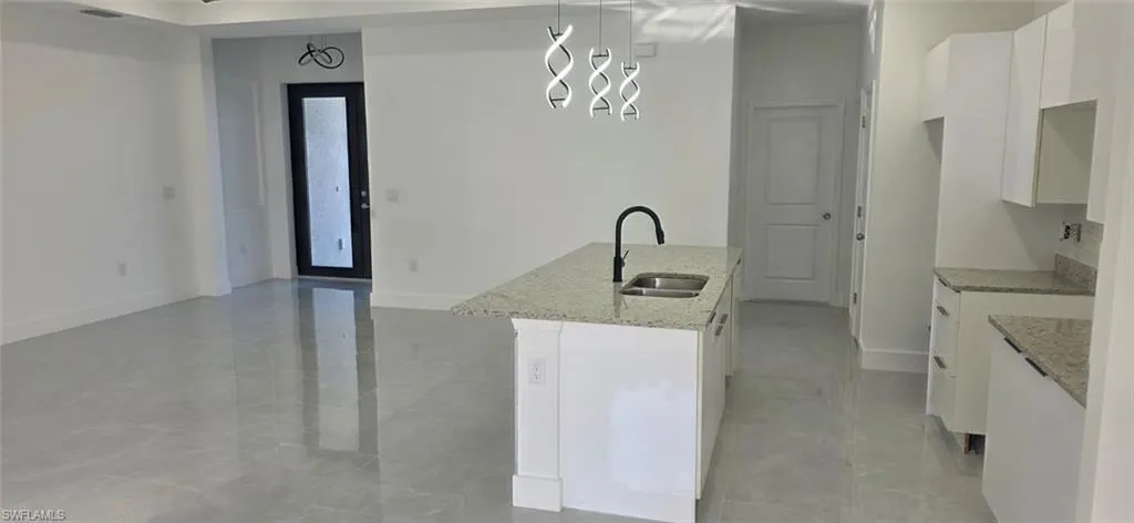 Kitchen featuring white cabinetry, light stone counters, a kitchen island with sink, and decorative light fixtures