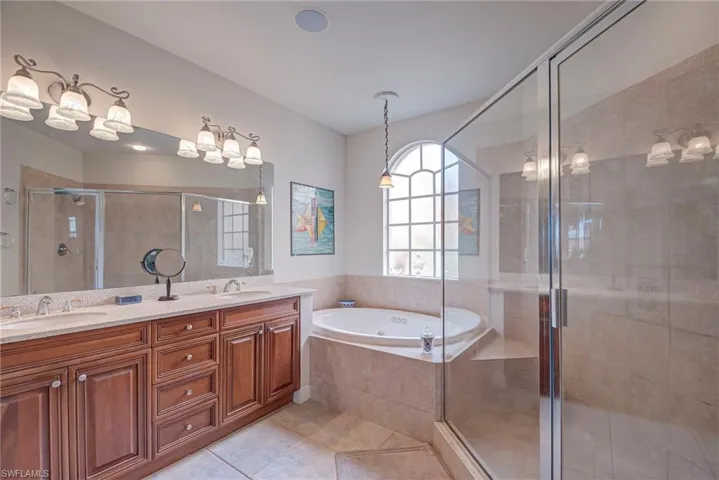Full bath with double vanity, a stall shower, a jetted tub, and light tile patterned floors