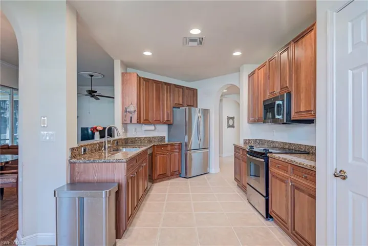 Kitchen featuring arched walkways, light stone counters, appliances with stainless steel finishes, brown cabinets, and light tile patterned floors