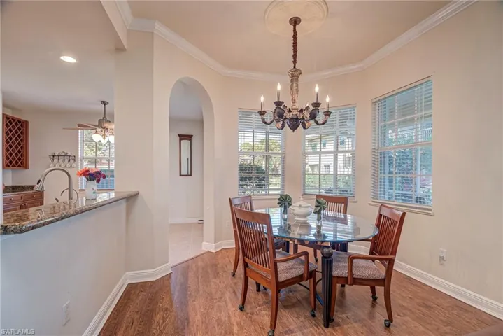 Dining area with wood finished floors, arched walkways, ornamental molding, and a chandelier
