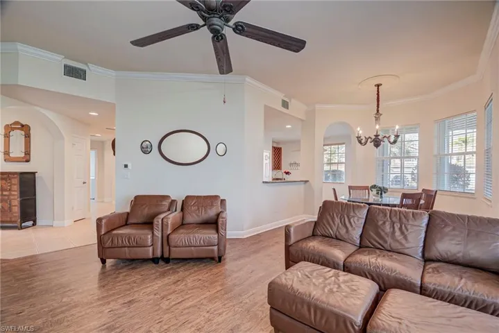 Living area with arched walkways, a chandelier, wood finished floors, ornamental molding, and ceiling fan