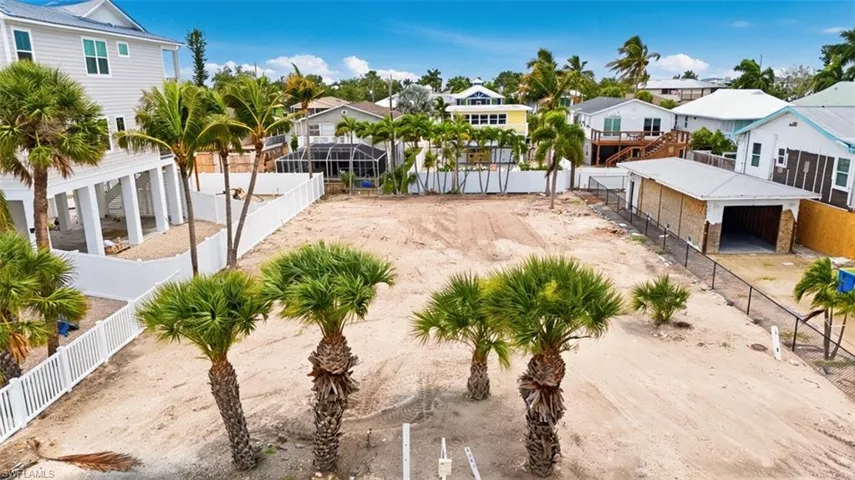 VIRTUALLY ENHANCED - Generous sandy lot featuring established palm trees and white vinyl fencing