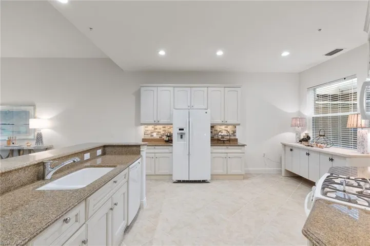 Kitchen featuring light stone countertops, white appliances, white cabinets, decorative backsplash, and recessed lighting