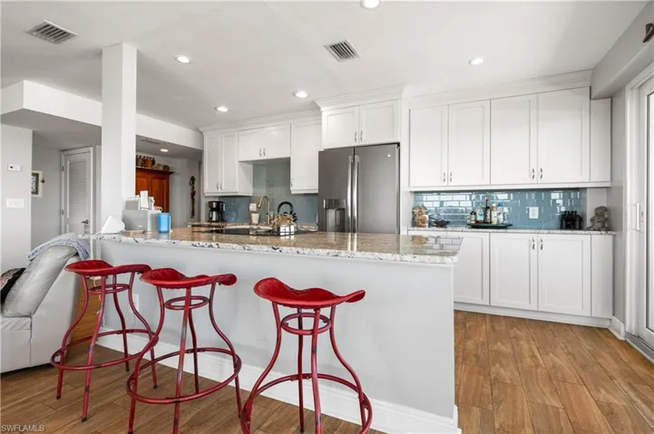 Kitchen with stainless steel fridge with ice dispenser, white cabinets, light stone counters, and light wood-type flooring