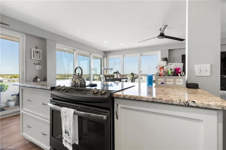 Kitchen with white cabinets, light stone counters, electric stove, and a wealth of natural light