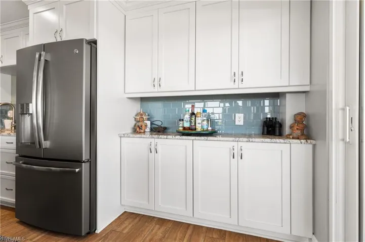 Bar with backsplash, stainless steel refrigerator with ice dispenser, light hardwood / wood-style flooring, light stone counters, and white cabinetry