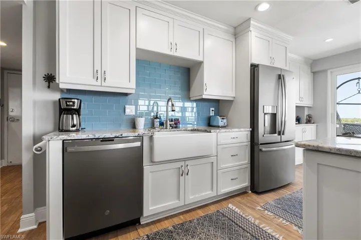 Kitchen with sink, light stone countertops, appliances with stainless steel finishes, light hardwood / wood-style floors, and white cabinetry