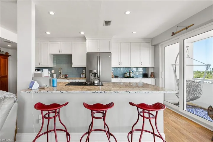 Kitchen featuring white cabinets, light hardwood / wood-style floors, light stone counters, and stainless steel refrigerator
