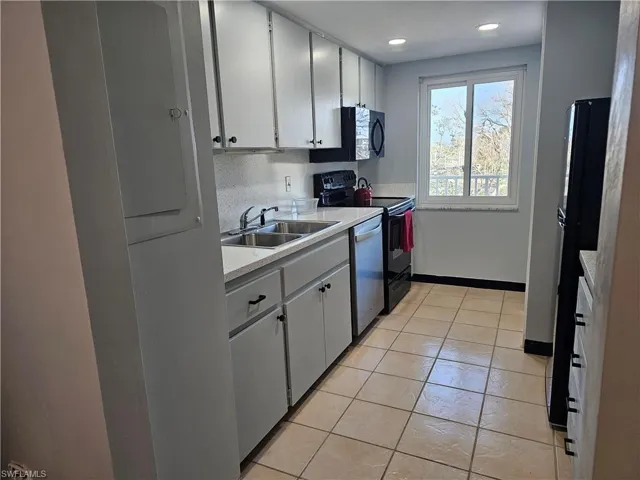Kitchen with light countertops, black appliances, light tile patterned floors, and white cabinets