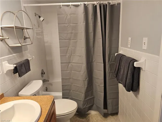Bathroom with tile walls, shower / bath combo, vanity, and wainscoting
