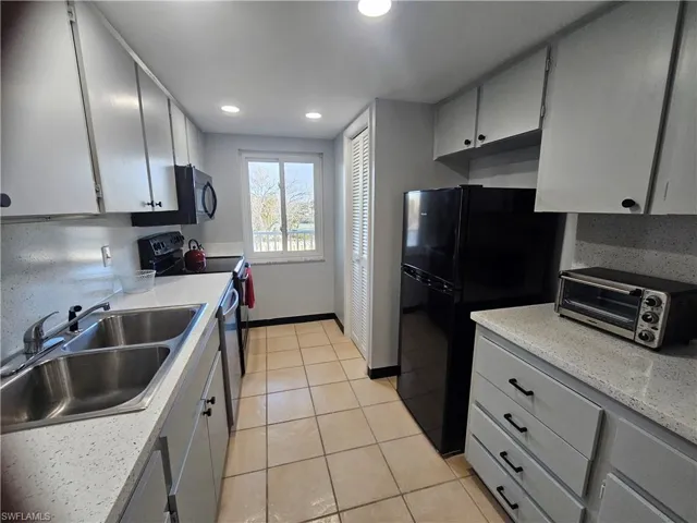Kitchen with stainless steel appliances, light tile patterned flooring, gray cabinets, recessed lighting, and light stone counters