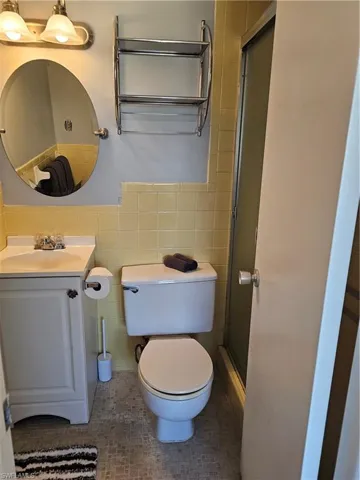 Full bathroom with a stall shower, vanity, tile walls, and a wainscoted wall