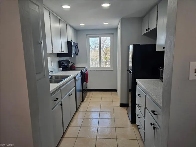 Kitchen featuring light countertops, light tile patterned floors, black appliances, recessed lighting, and white cabinets