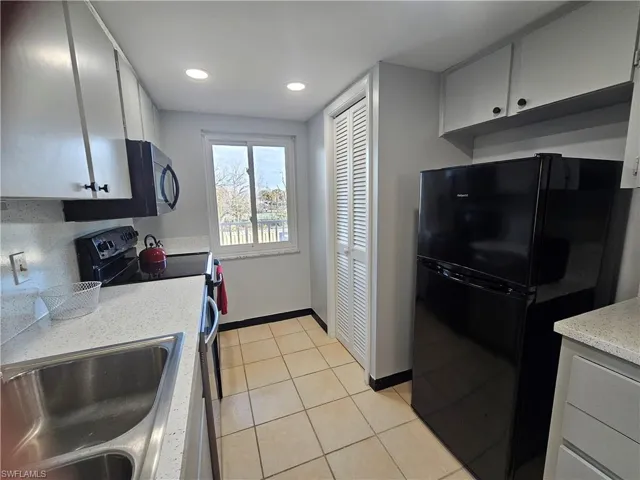 Kitchen featuring black appliances, light tile patterned floors, recessed lighting, light stone countertops, and white cabinets