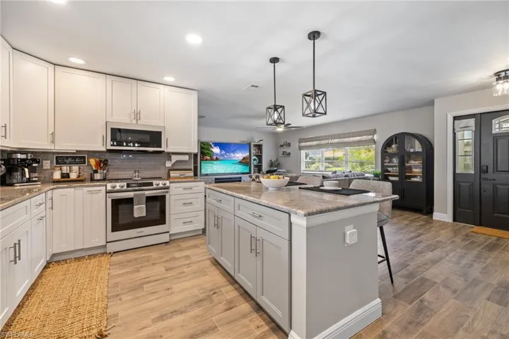 Kitchen with white cabinetry, light stone counters, a kitchen island, decorative light fixtures, and stainless steel electric stove