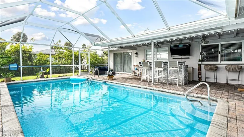 View of swimming pool featuring ceiling fan, a patio, an outdoor bar, and glass enclosure