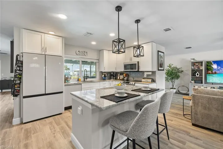 Kitchen with white cabinetry, a center island, light hardwood / wood-style flooring, appliances with stainless steel finishes, and light stone countertops