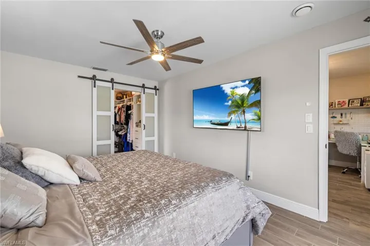 Bedroom with ceiling fan, light hardwood / wood-style floors, a barn door, a walk in closet, and a closet