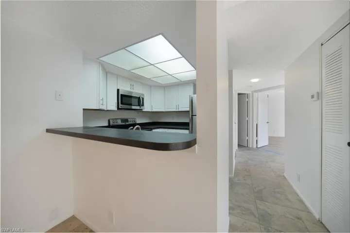 Kitchen with kitchen peninsula, appliances with stainless steel finishes, a textured ceiling, white cabinets, and light tile patterned flooring