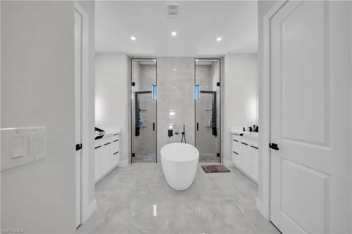 Bathroom featuring a freestanding soaking tub, dual glass-enclosed showers, two integrated vanity sinks, and large format tile flooring