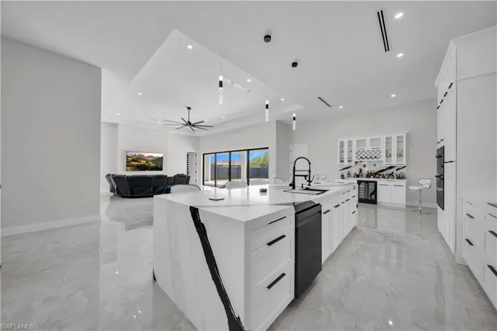 Kitchen featuring a large waterfall island with integrated sink, white cabinetry with black hardware, double wall ovens, and a dedicated beverage station