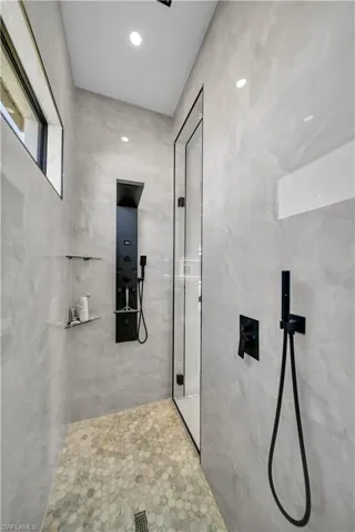 Walk-in shower featuring large format tiled walls, a pebble-tiled floor, a matte black multi-function shower panel, and a clear glass shower enclosure