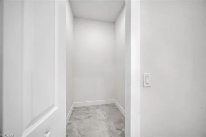 Recessed interior space with light gray marble-look tile flooring and crisp white baseboards