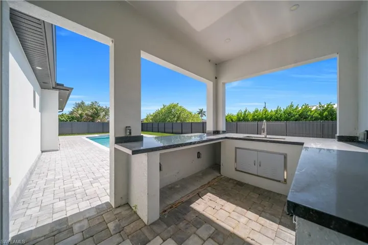 Outdoor kitchen featuring dark stone countertops and an integrated sink with a contemporary faucet