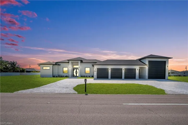 Contemporary exterior featuring a paver driveway, four garage doors, and a double-door entry with decorative wrought iron