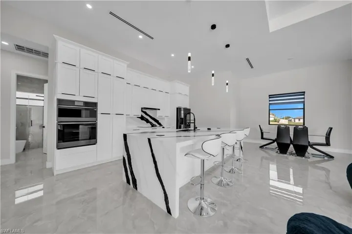 Gourmet kitchen featuring a waterfall island with dramatic veining, integrated double ovens, white shaker cabinetry with black hardware, and pendant lighting